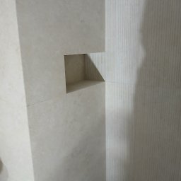 BCS - Wykończona wnęka w łazience wyłożonej beżowymi płytkami w Kłobucku. Widoczne pionowe żłobienia na ścianie i precyzyjne łączenia płytek.