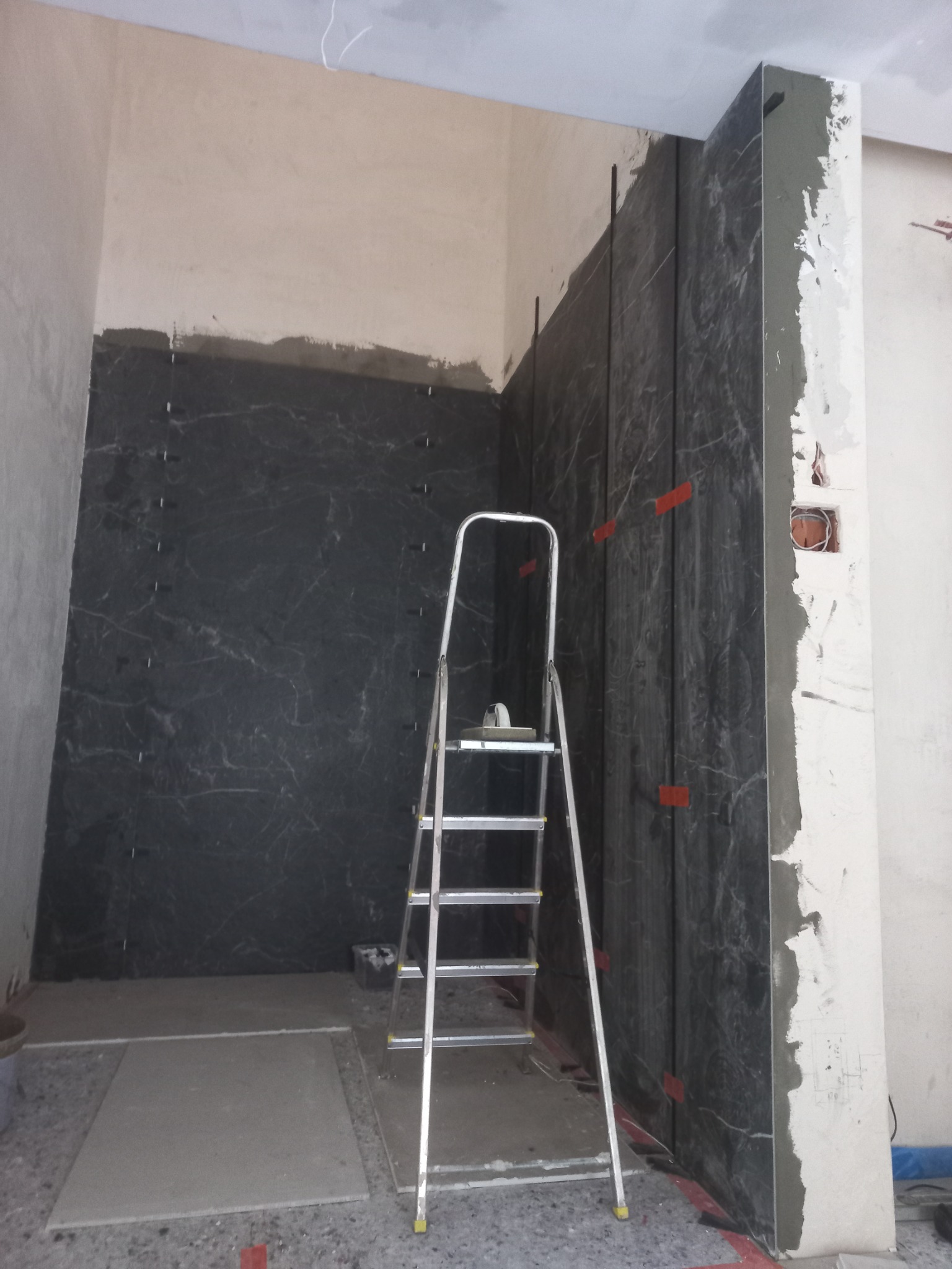 Częściowo wyłożona marmurowymi płytkami ściana w łazience z drabinką i narzędziami glazurniczymi. Widoczny surowy stan wykończenia.