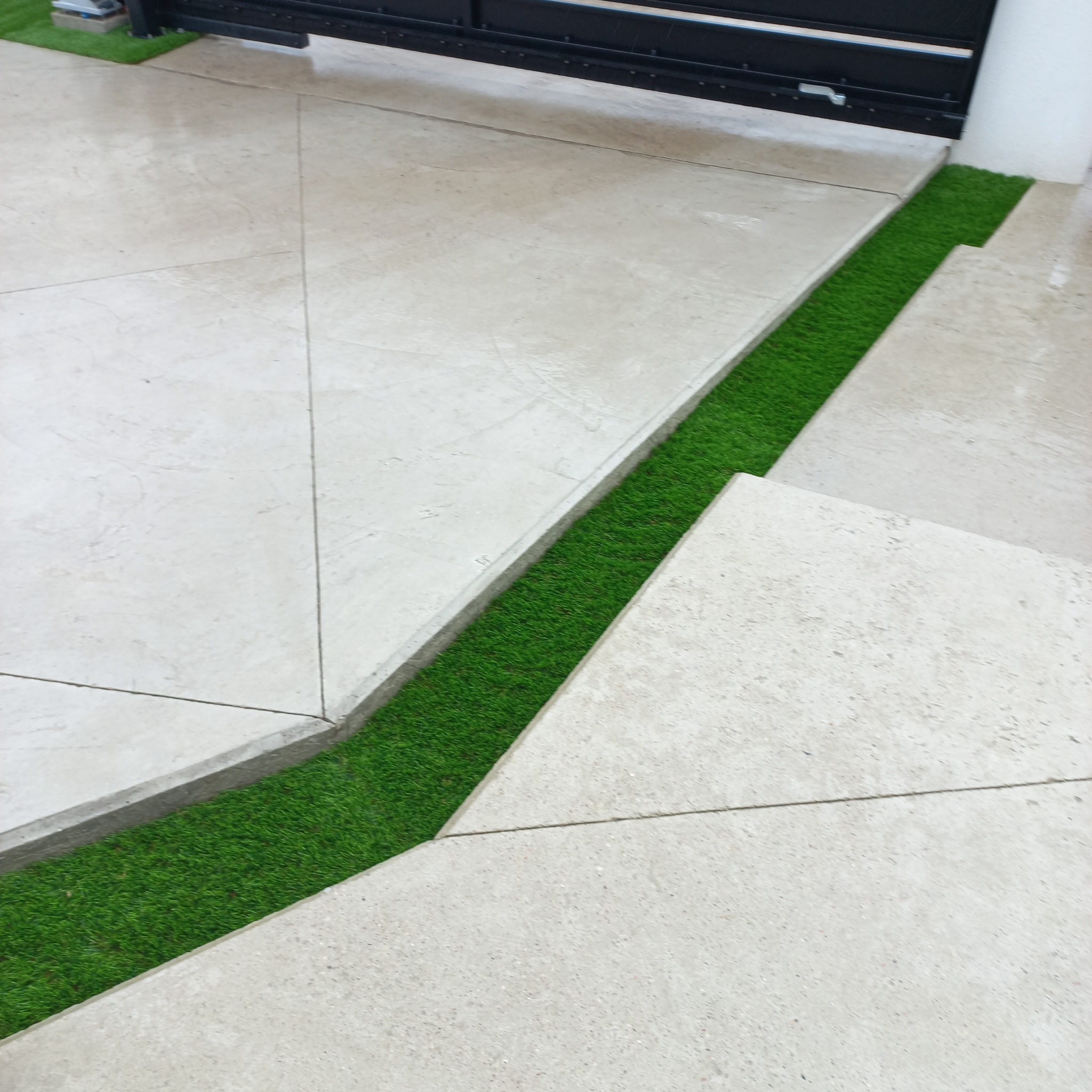 Nowoczesna aranżacja: jasnoszara betonowa posadzka z geometrycznym wzorem i wstawkami ze sztucznej trawy. Minimalistyczny design przy bramie.