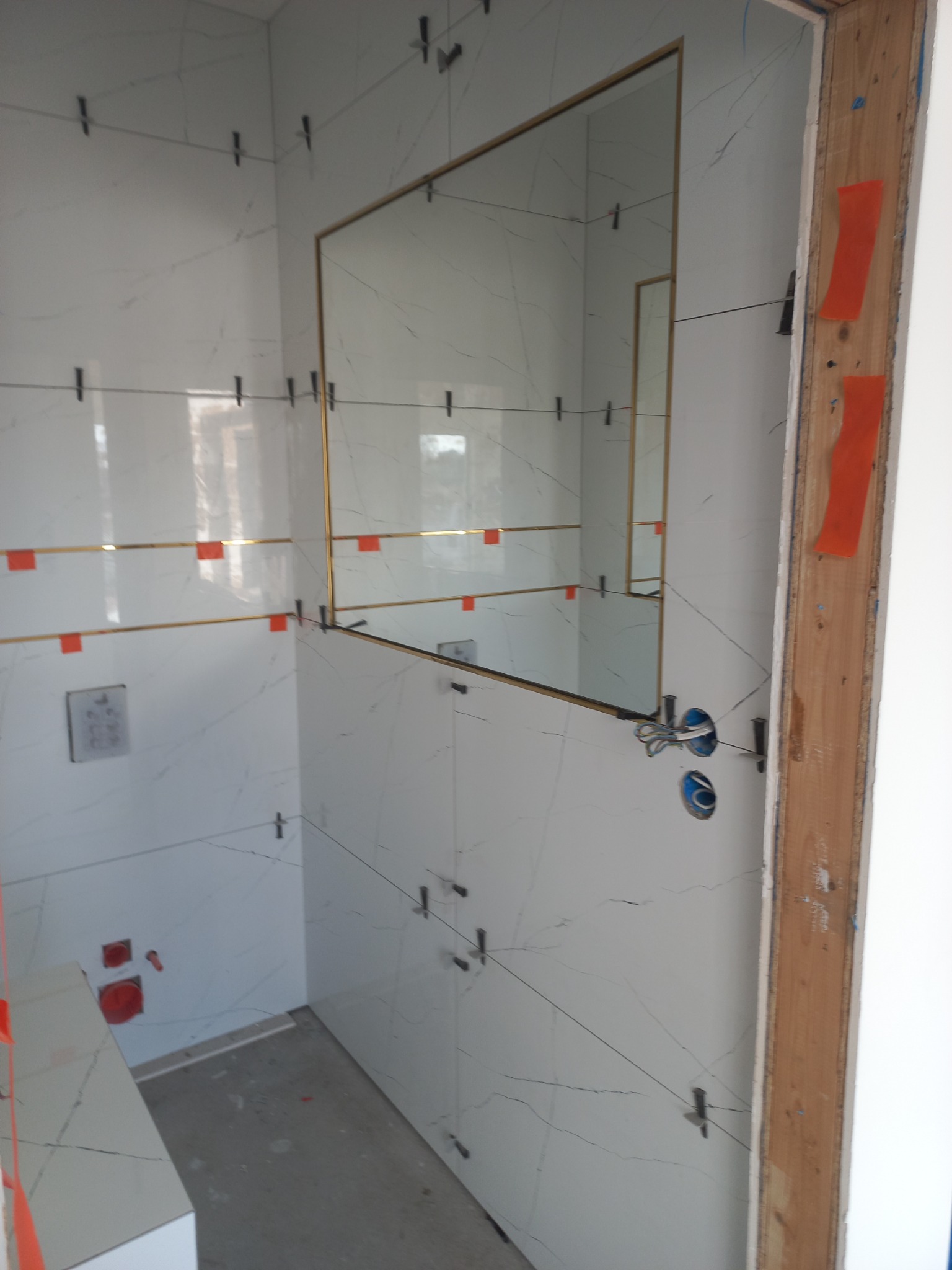 Białe płytki imitujące marmur z złotymi listwami, zamontowane z użyciem klipsów poziomujących, instalacja elektryczna w łazience w trakcie wykończenia.