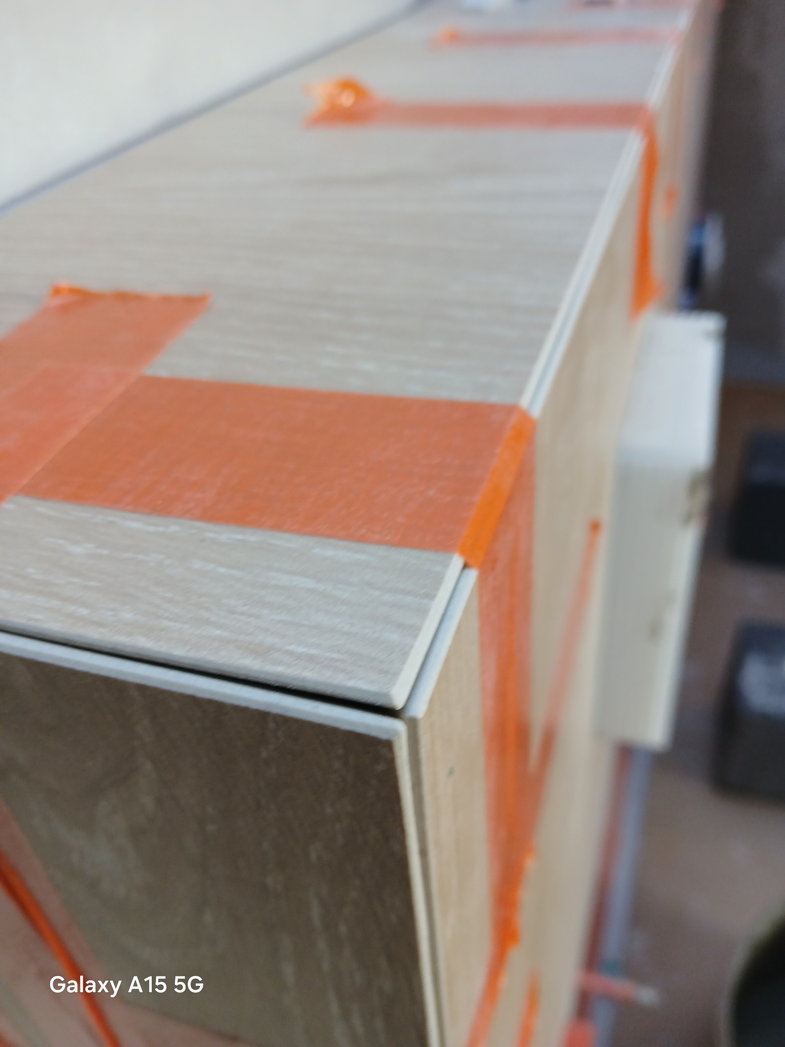 Wykończona obudowa wanny z płytek imitujących drewno, zabezpieczona pomarańczową taśmą malarską. Widoczne fugi i krawędzie płytek.