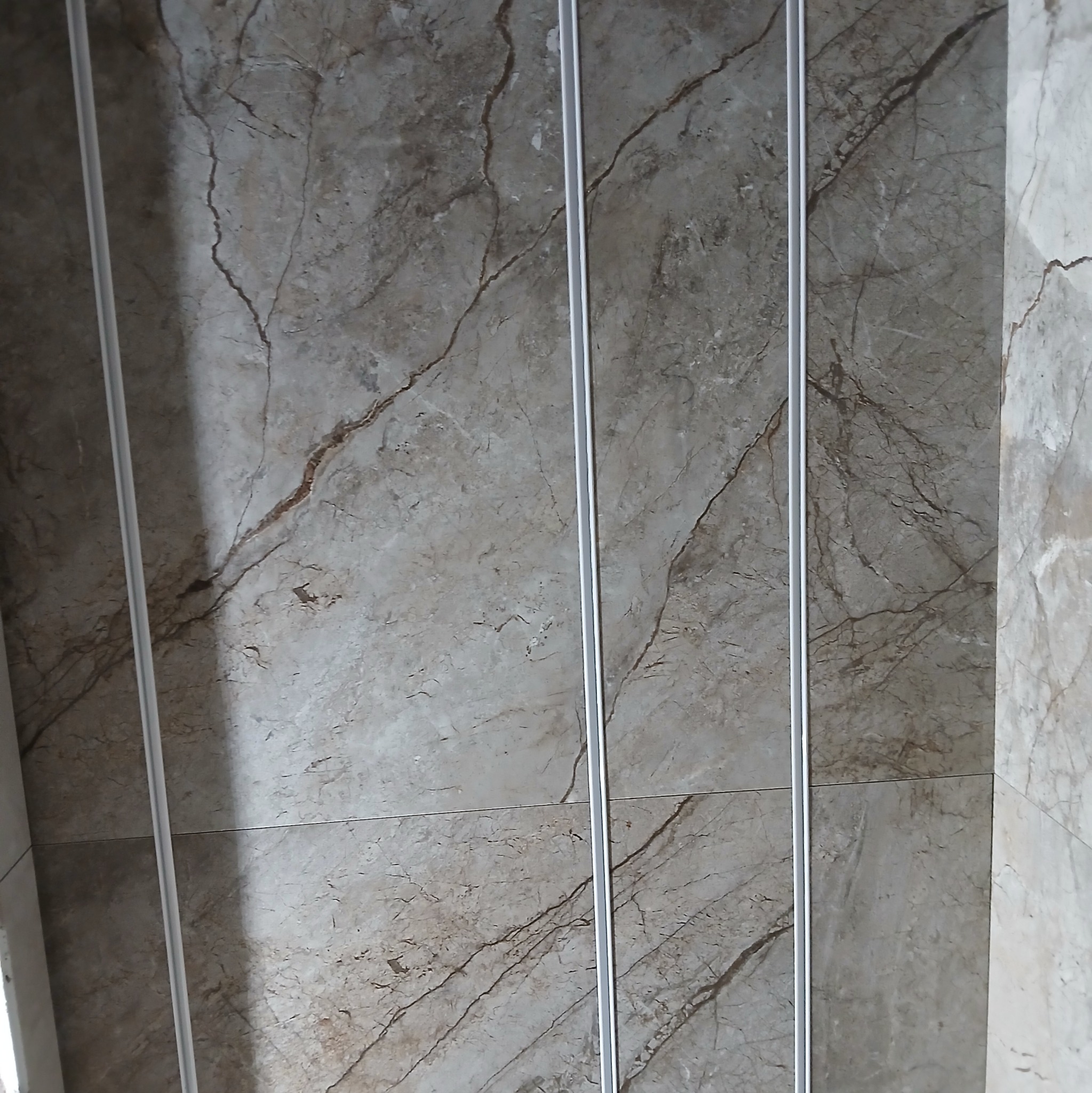 Ułożone płytki imitujące marmur z wąskimi, srebrnymi listwami dekoracyjnymi. Widok z góry, podkreślający wzór i precyzję wykonania. Jasne, neutralne kolory.