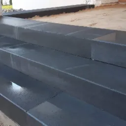Nowe, ciemnoszare, betonowe schody wejściowe, świeżo po ułożeniu, z widocznymi drobnymi kamieniami kostki brukowej obok i śladami wilgoci.