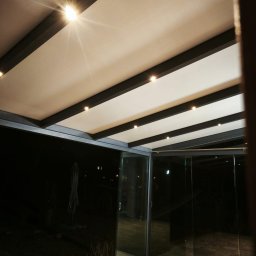 MATEUSZ KALISZUK TechRol - Nowoczesna pergola metalowa z oświetleniem LED, widok od dołu, szklane ściany przesuwne, nocne ujęcie.