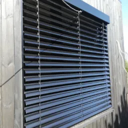 Zamknięte, poziome, czarne żaluzje fasadowe zamontowane na elewacji budynku z drewnianych desek.