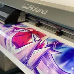 Drukarka wielkoformatowa Roland w trakcie drukowania grafiki anime z przewagą kolorów różowego, fioletowego i niebieskiego.