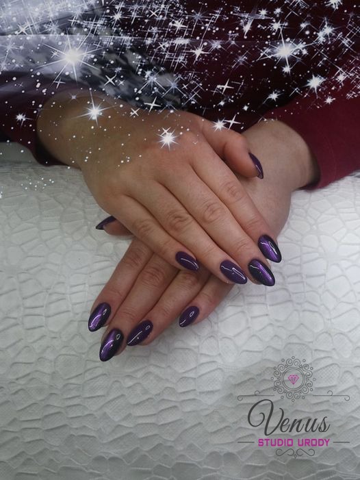 Dłonie kobiety z ciemnofioletowym manicurem w stylu 'kocie oko', ułożone na białym teksturowanym podłożu; widoczne logo salonu urody i delikatne efekty świetlne.
