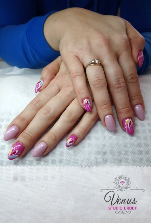 Dłonie kobiety z pomalowanymi paznokciami: fuksjowe z abstrakcyjnym, kolorowym wzorem i jasnoróżowe, na serdecznym palcu złoty pierścionek z oczkiem.
