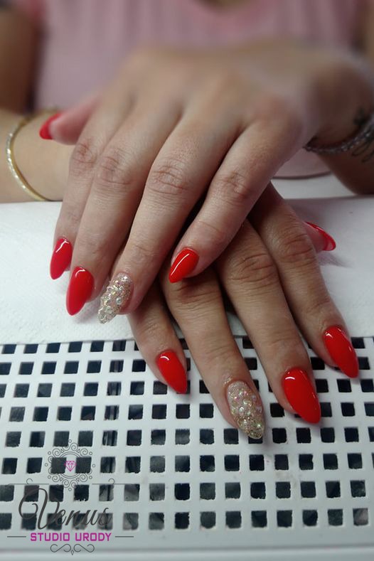 Dłonie z czerwonym manicure hybrydowym i jednym paznokciem zdobionym brokatem, ułożone na białej lampie UV do paznokci.