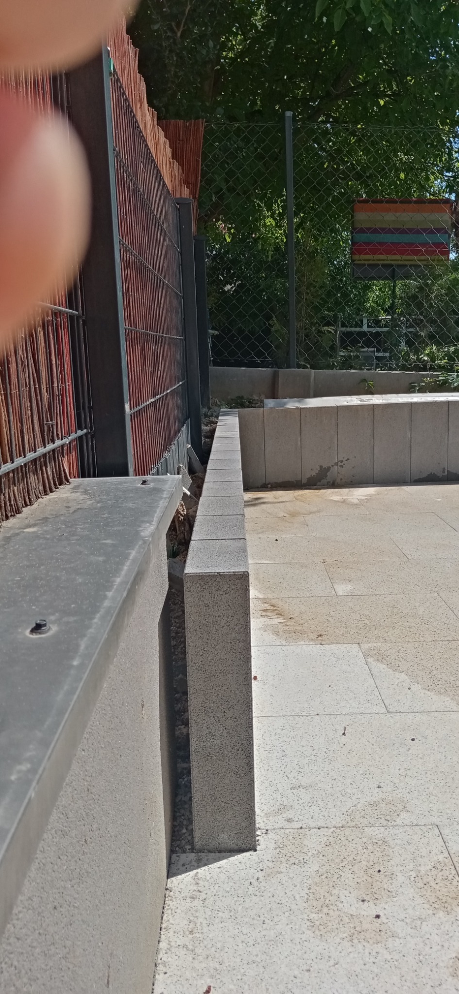 Fragment ogrodzenia z paneli z brązowej wikliny i metalowej siatki, z betonowymi słupkami i kostką brukową na podłożu.