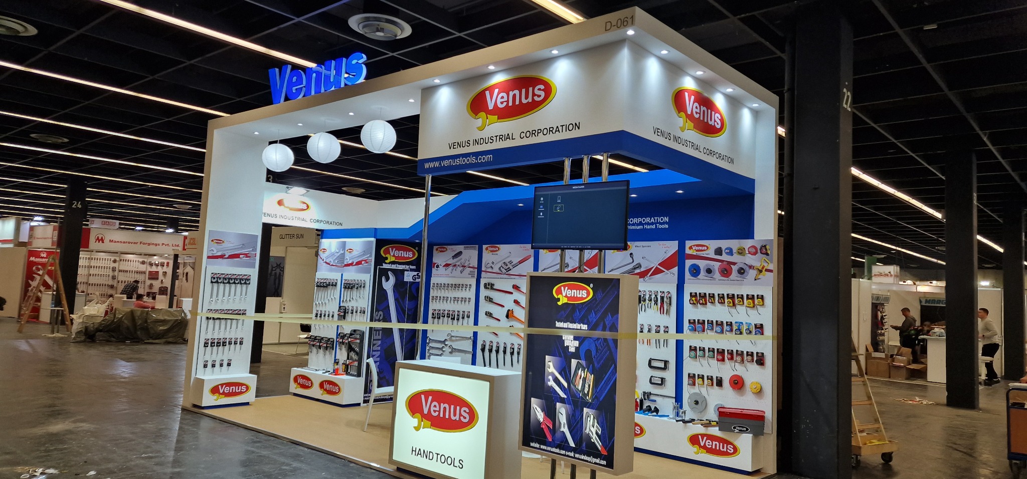 Stoisko targowe firmy Venus Industrial Corporation z ekspozycją narzędzi ręcznych, oświetlone lampami kulami, z logo firmy i ekranem prezentacyjnym.