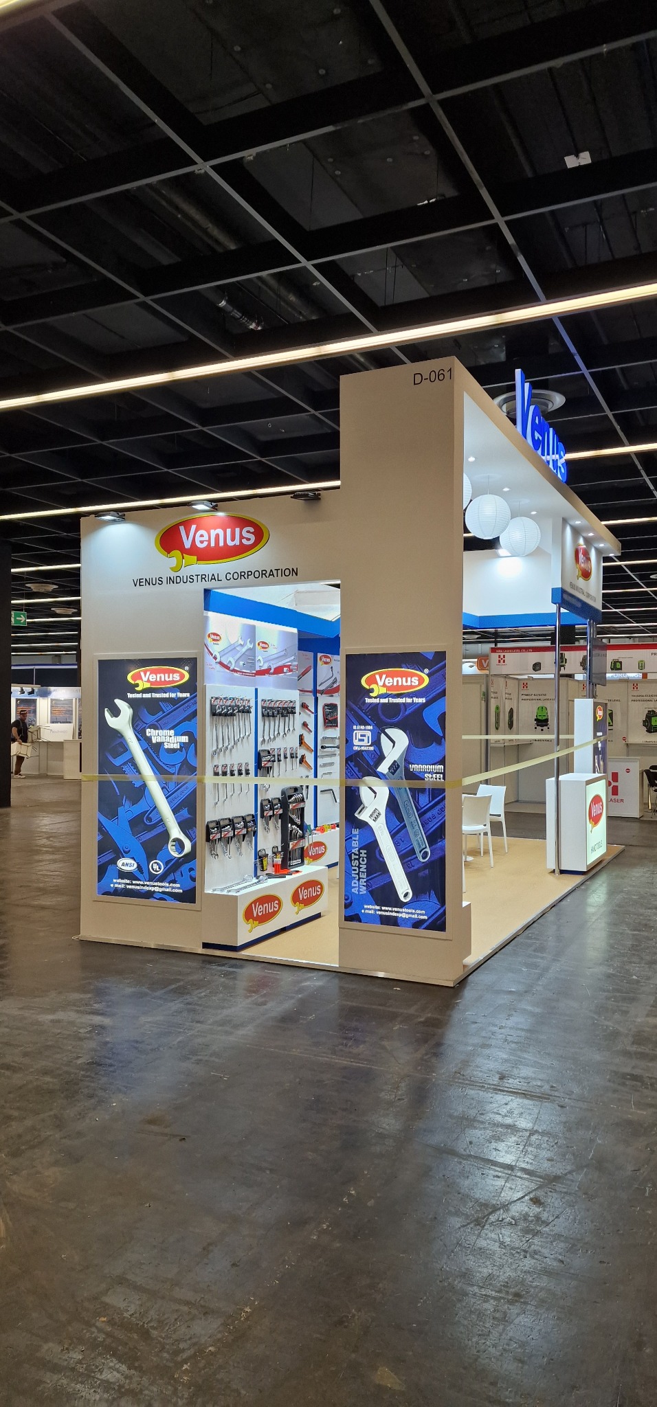 Stoisko targowe firmy Venus Industrial Corporation z narzędziami, prezentujące klucze nastawne i inne narzędzia, oświetlone kulistymi lampami, z numerem stoiska D-061.