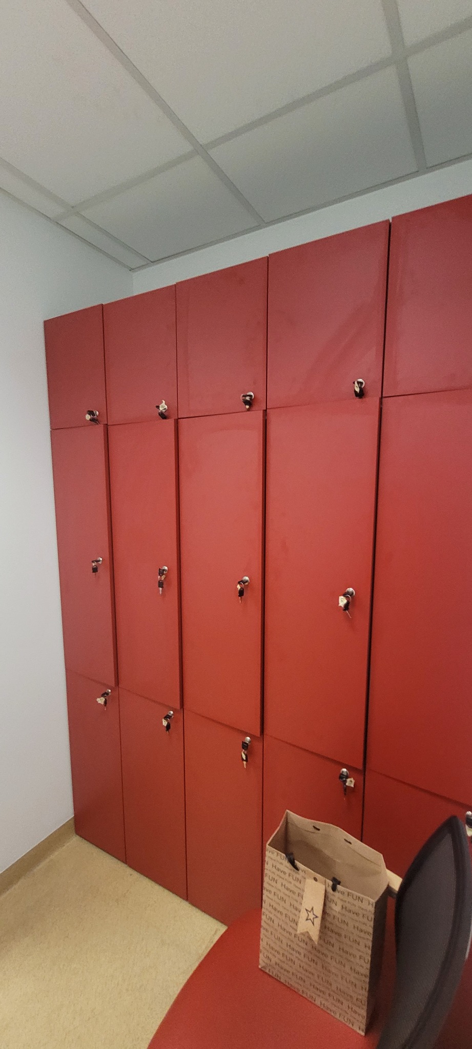 Czerwone szafki zamykane na klucz, ustawione rzędem w jasnym pomieszczeniu, obok stoi torebka prezentowa z napisem Have FUN