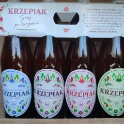 Cztery butelki napoju słodowego w kartonowym opakowaniu, każdy wariant smakowy oznaczony etykietą z ludowym motywem: jabłko-mięta, gruszka-czarny bez-limonka, róża-malina-czarna porzeczka...