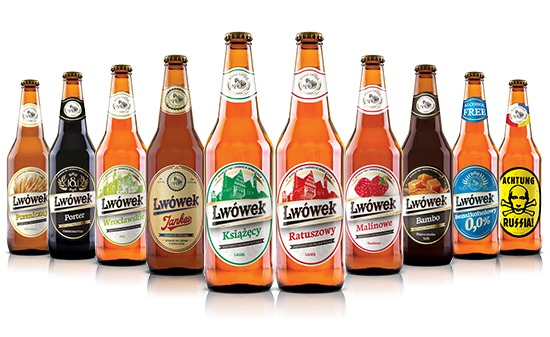 Różne rodzaje piwa Lwówek w szklanych butelkach z etykietami, ustawione w rzędzie na białym tle, prezentujące pełną gamę smaków, od jasnych lagerów po ciemne portery i piwa owocowe.