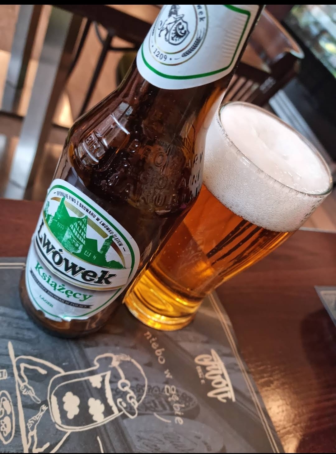 Butelka piwa Lwówek Książęcy obok szklanki z piwem na stoliku z menu.