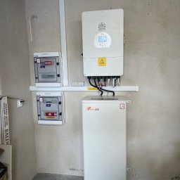 Sunrise-Technology JAKUB WITOS - Instalacja magazynu energii FelicityESS i falownika Deye w Milówce, z rozdzielnicami elektrycznymi. Widoczne okablowanie i surowa ściana w tle.