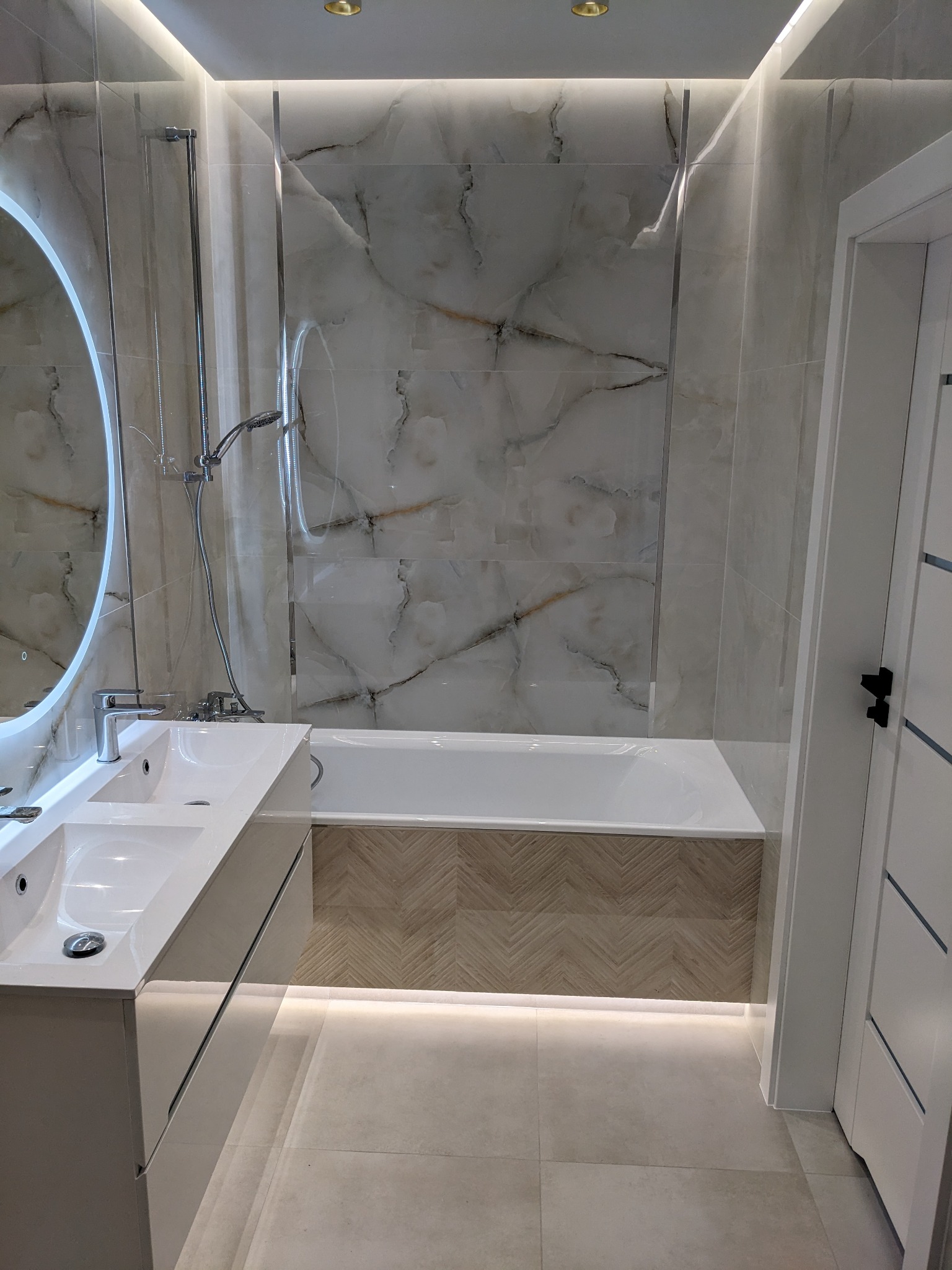 Nowoczesna łazienka z marmurowymi płytkami, podświetlanym lustrem i umywalką nablatową, wykończona w jasnych barwach.