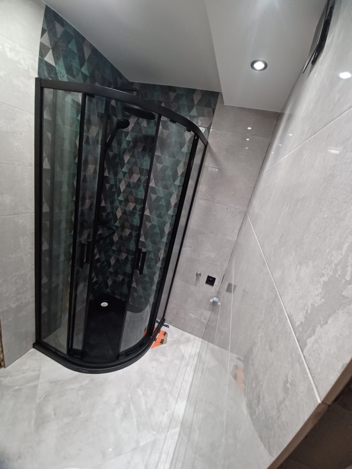 Nowoczesna kabina prysznicowa z czarnymi profilami w wyremontowanej łazience w Bydgoszczy, z geometryczną tapetą na ścianie i jasnymi, dużymi płytkami na podłodze.