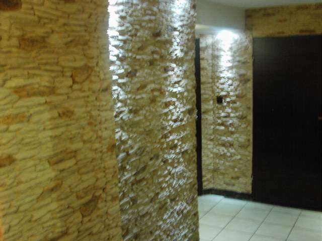 Fragment wnętrza z dekoracyjną ścianą z kamienia naturalnego i białą podłogą z płytek, widoczna czarna futryna drzwi.