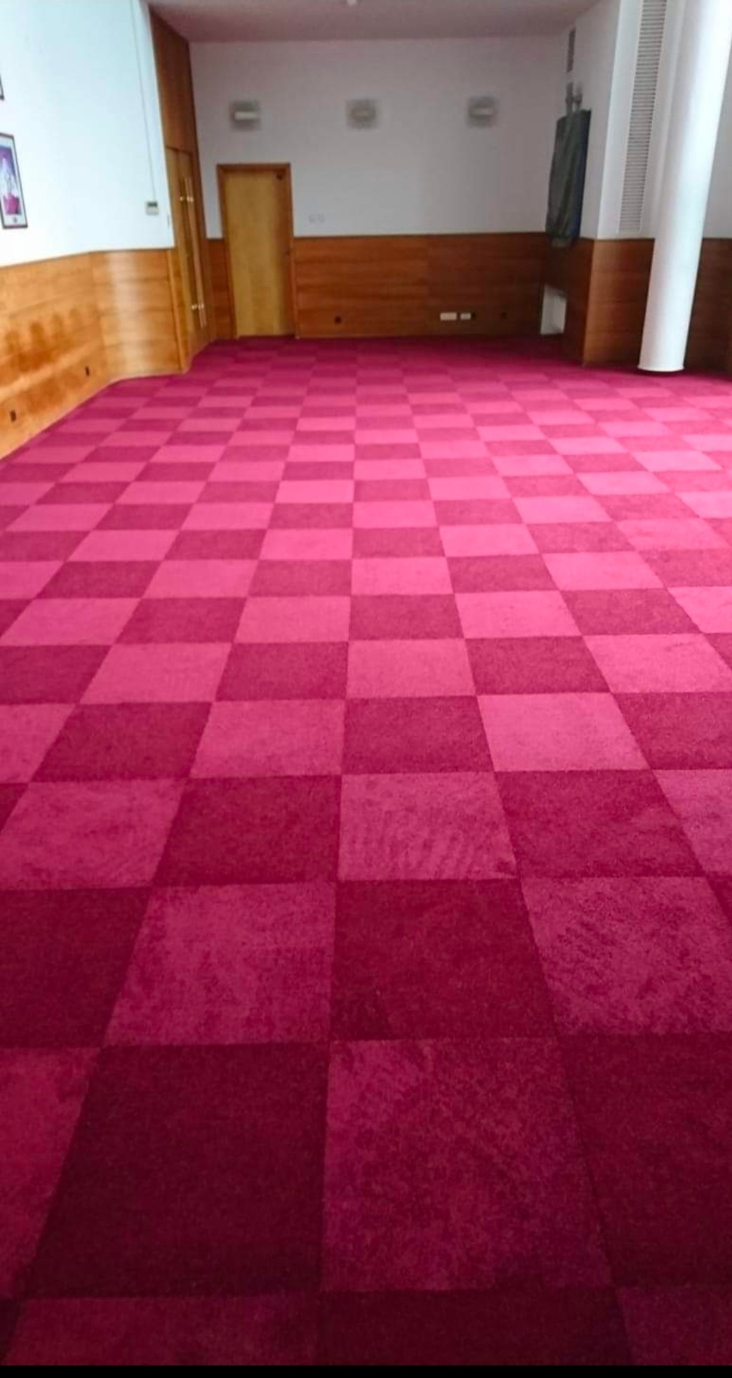 Czerwona wykładzina dywanowa w szachownicę w przestronnym pomieszczeniu z drewnianą boazerią i białymi ścianami.