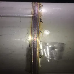 Spoina na rurze ze stali nierdzewnej, widoczne ślady obróbki i przebarwienia termiczne.