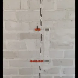 Surowa ściana z betonu komórkowego z wyżłobionymi pionowymi bruzdami na przewody elektryczne, widoczne pomarańczowe puszki instalacyjne w rzędzie i podwójnie oraz poziome rury karbowane przy podłodze.