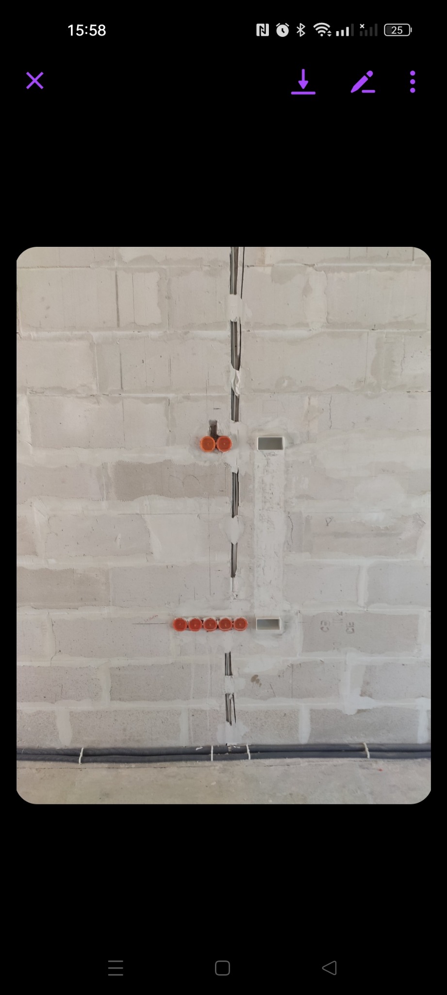 Surowa ściana z betonu komórkowego z wyżłobionymi pionowymi bruzdami na przewody elektryczne, widoczne pomarańczowe puszki instalacyjne w rzędzie i podwójnie oraz poziome rury karbowane przy podłodze.