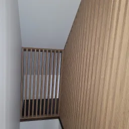 Drewniana ścianka działowa z pionowych listew w jasnym odcieniu dębu, oddzielająca schody od korytarza, widok z góry.