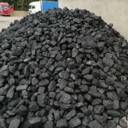 Góra czarnego węgla kamiennego na placu składowym, z widocznymi w tle samochodami ciężarowymi.