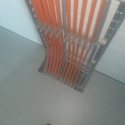 ECOELECTRIC POLAND SPÓŁKA Z OGRANICZONĄ ODPOWIEDZIALNOŚCIĄ - Pomarańczowe i szare przewody ułożone równolegle w metalowej korycie kablowej, widok z góry, fragment stopy w skarpetce w rogu kadru.