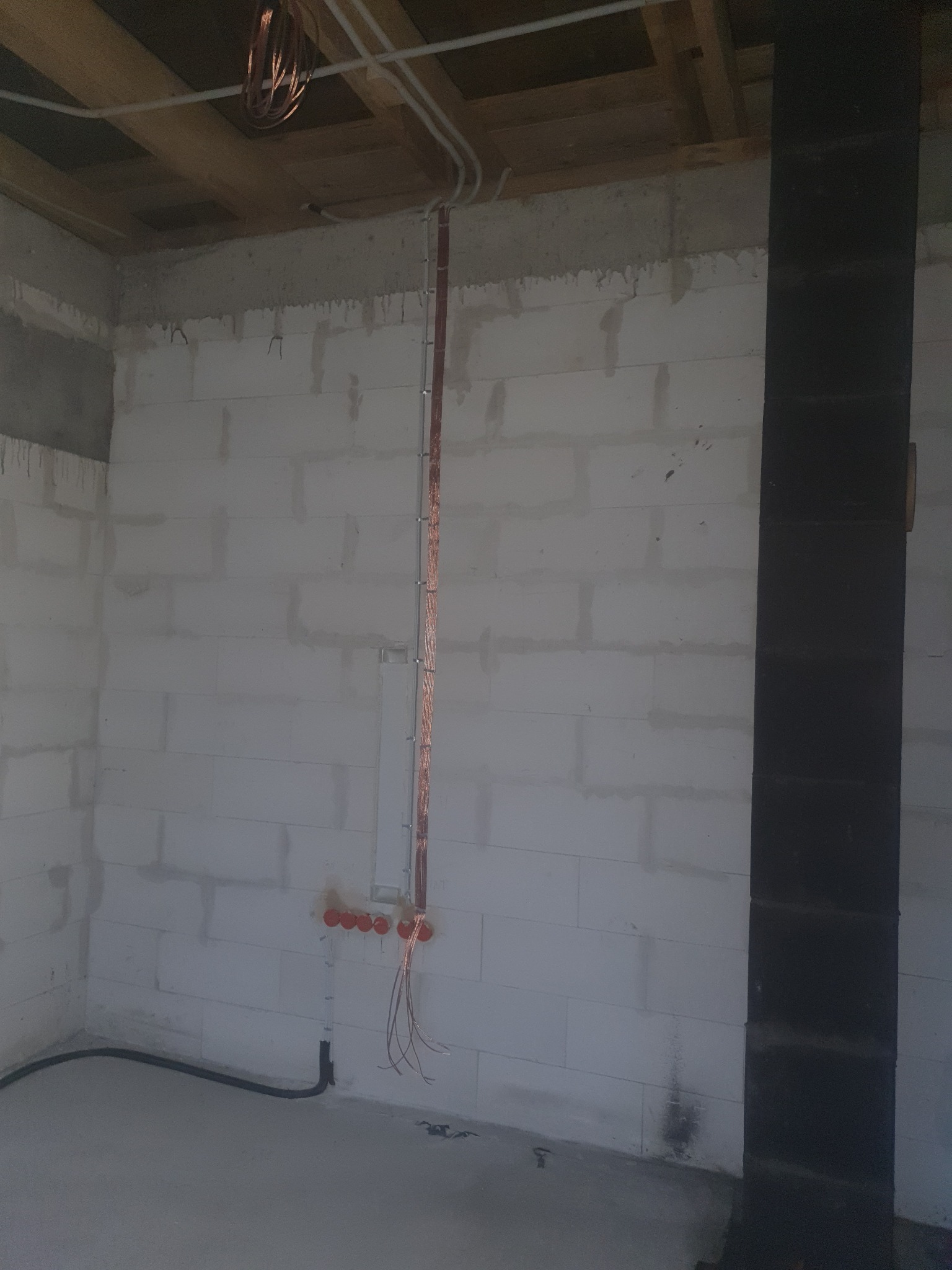 Surowy stan instalacji elektrycznej w nowym budynku: widoczne kable prowadzone po ścianie z betonu komórkowego, puszki instalacyjne w rzędzie oraz rurki PCV pod sufitem, zwisająca wiązka przewodów...
