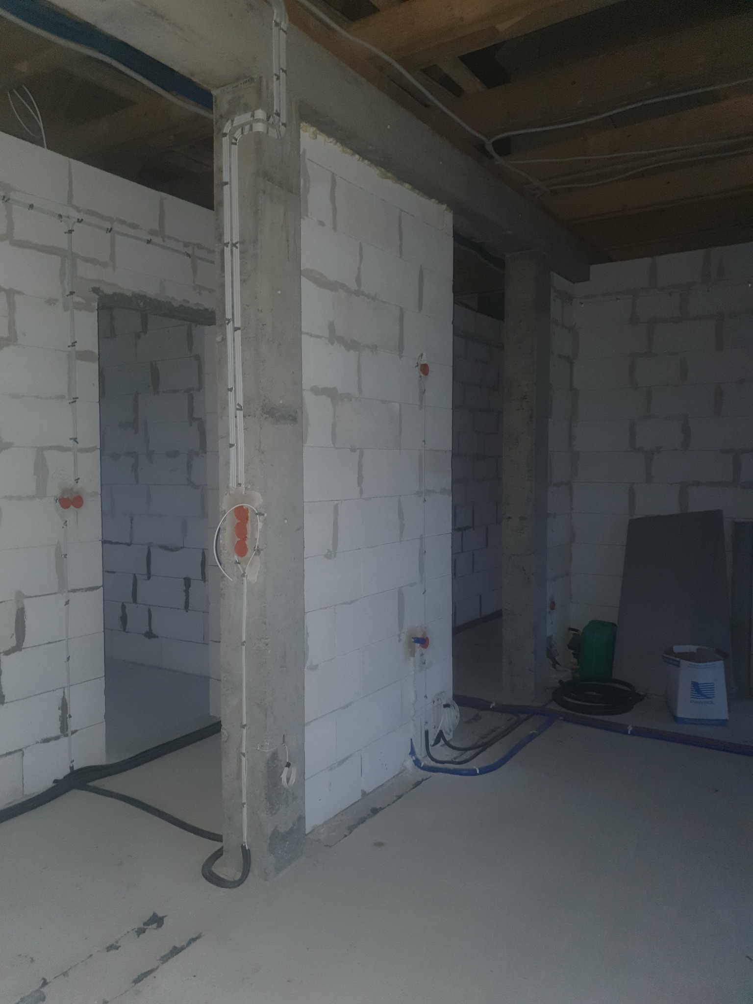 Surowy stan wnętrza budynku z widoczną instalacją elektryczną w rurkach PCV, zamontowaną na ścianach z betonu komórkowego, z widocznymi puszkami elektrycznymi i przewodami ułożonymi w bruzdach...