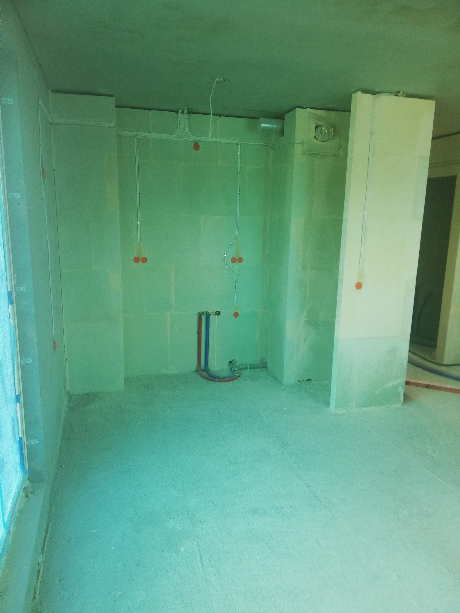 Surowy stan wnętrza z widocznymi przewodami elektrycznymi, puszkami instalacyjnymi i rurami wodnymi przed wykończeniem ścian.