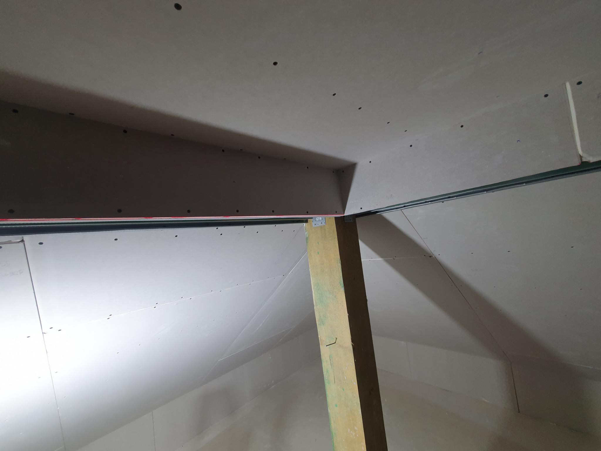 Poddasze z ukończoną konstrukcją z płyt gipsowo-kartonowych, widoczny drewniany słup podtrzymujący, szpachlowane łączenia płyt, przygotowane do dalszych prac wykończeniowych.