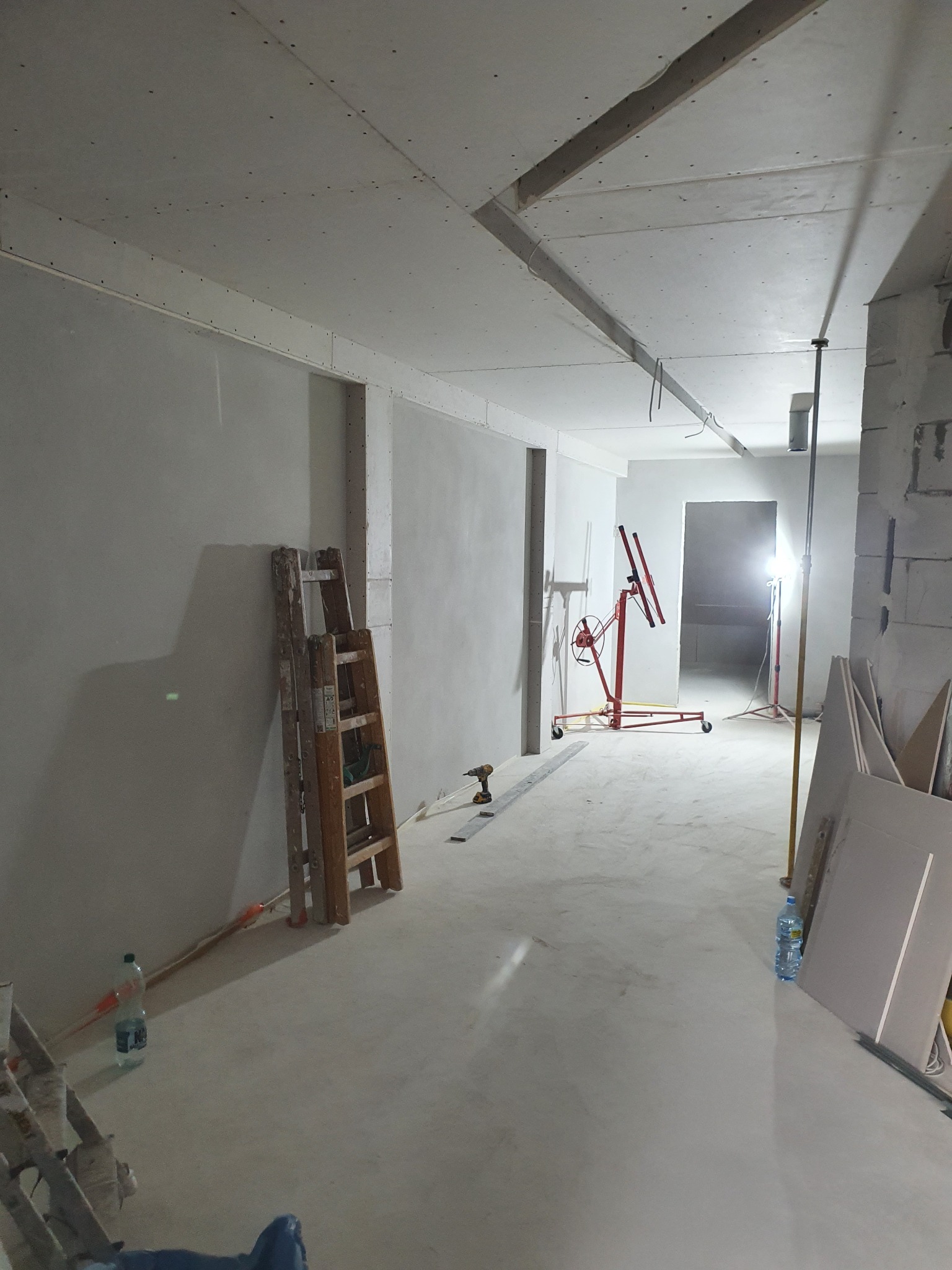 Wnętrze w trakcie prac wykończeniowych: zamontowane płyty gipsowo-kartonowe na suficie i ścianach, widoczna drabina, podnośnik do płyt i narzędzia, przygotowane do dalszych prac.