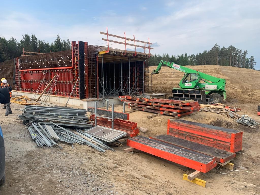 Budowa konstrukcji żelbetowej z użyciem szalunków i zbrojenia, widoczny dźwig teleskopowy i elementy konstrukcyjne na placu budowy.