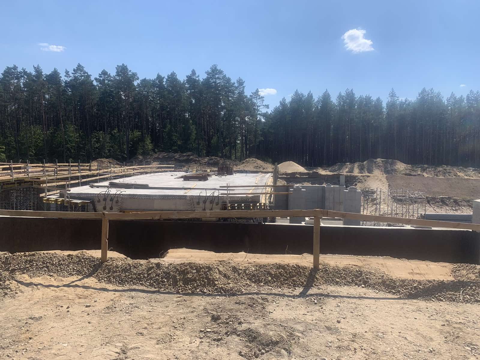 Wylewanie fundamentów z betonu z widocznymi zbrojeniami na tle lasu i nieba.