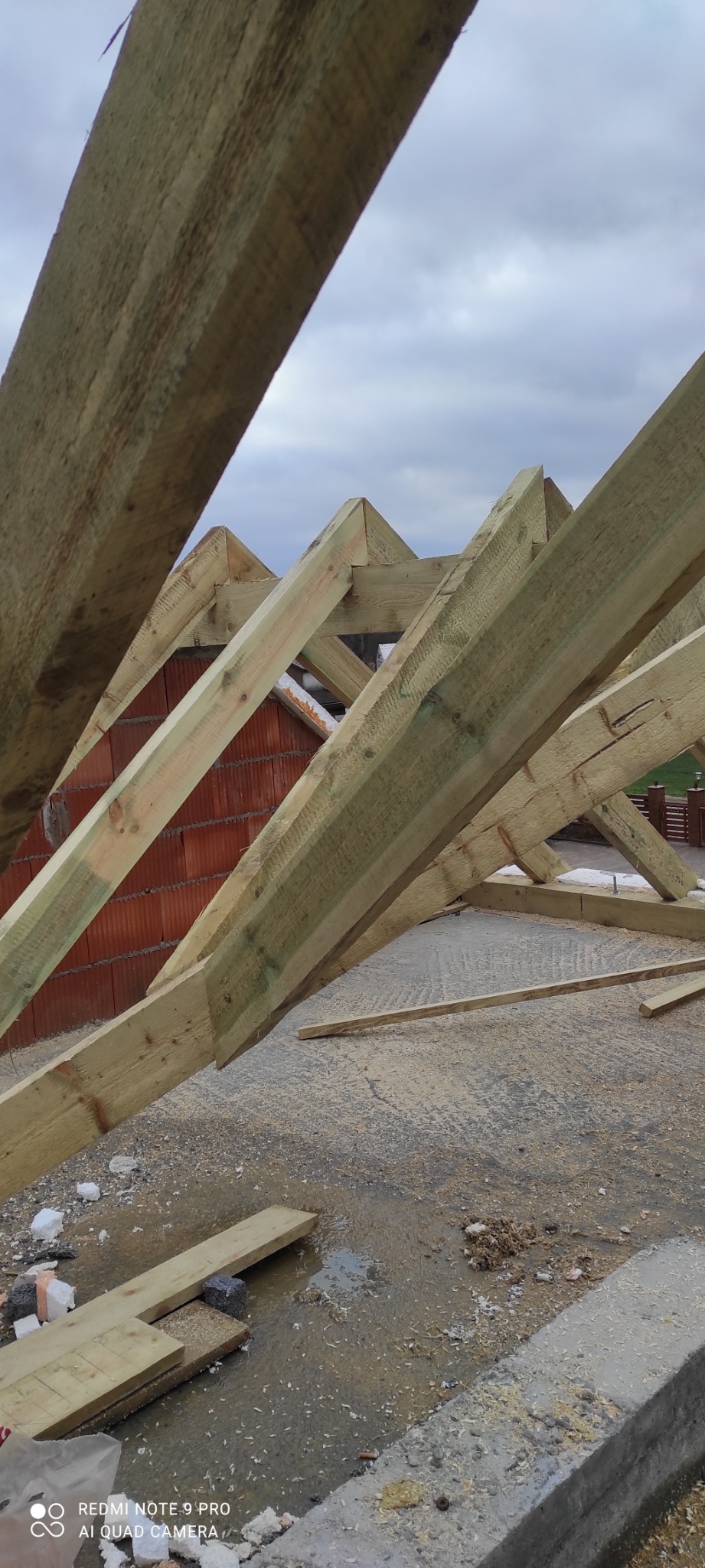 Konstrukcja drewniana więźby dachowej na etapie budowy, widoczne cegły w tle i fragment nieba.