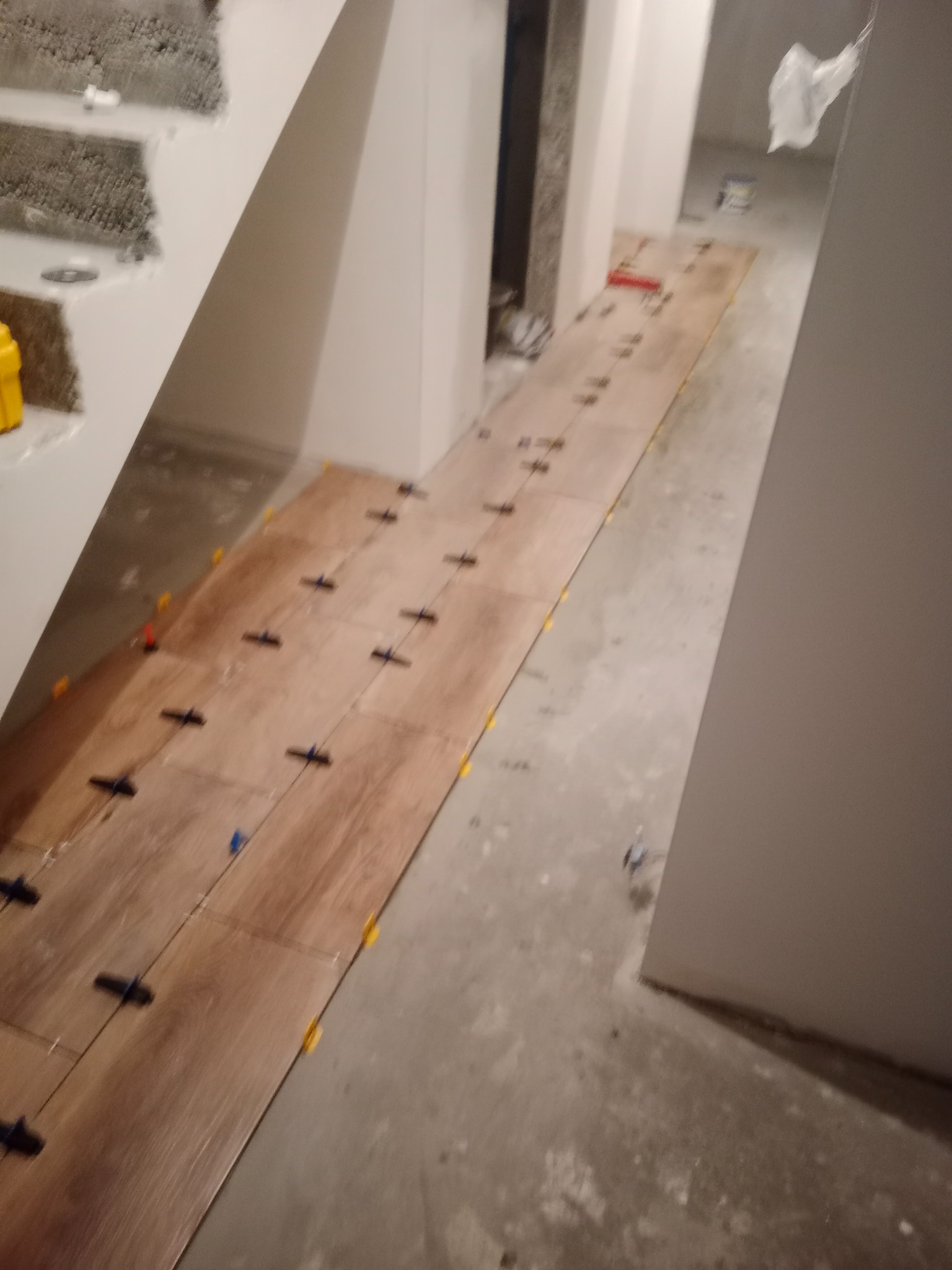 Układanie drewnopodobnych płytek podłogowych w korytarzu, z użyciem poziomujących klipsów i klinów dystansowych.