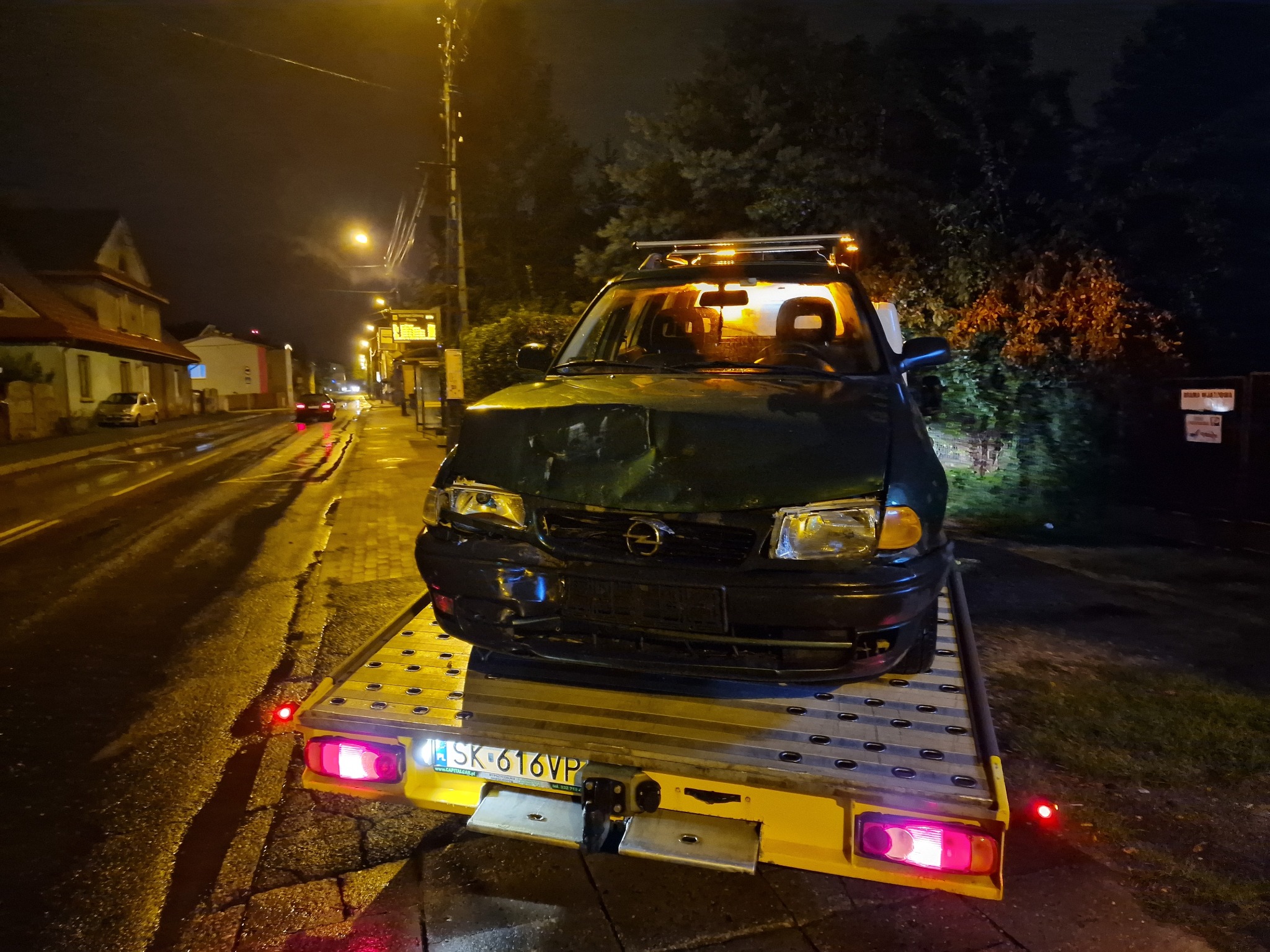 Uszkodzony, ciemnozielony Opel Astra na żółtej lawecie w nocnej scenerii miejskiej, widoczne wgniecenia na masce i reflektory. Tablica rejestracyjna SK 616VP.