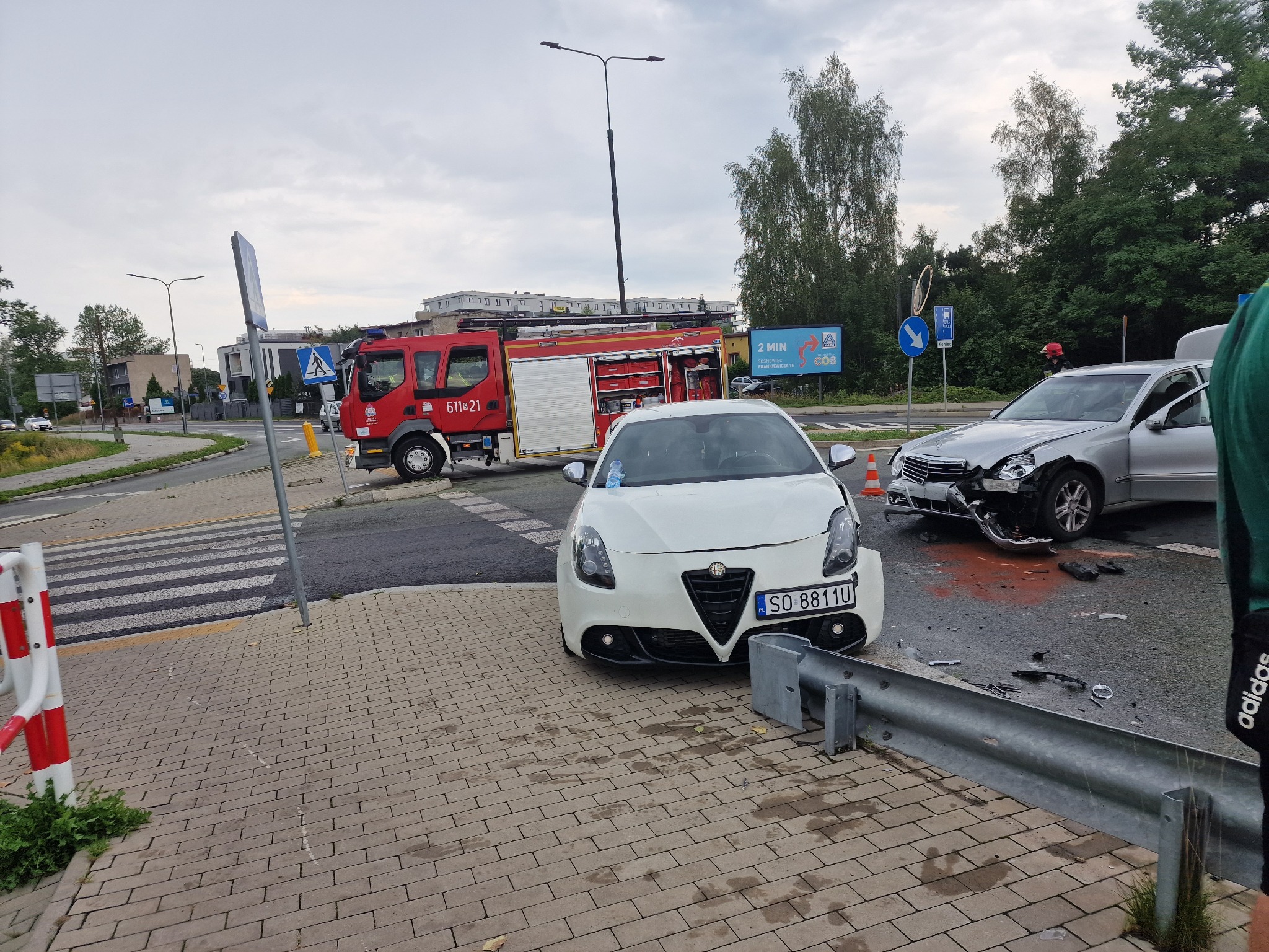 Uszkodzone w wyniku kolizji Alfa Romeo Giulietta i Mercedes na skrzyżowaniu, w tle wóz strażacki z włączonymi światłami.