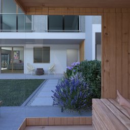 MB- Projektowanie ogrodów - Widok z drewnianej sauny w Radomierzycach na nowoczesny ogród z kwitnącą lawendą, trawnikiem i ścieżką z płyt betonowych prowadzącą do domu.