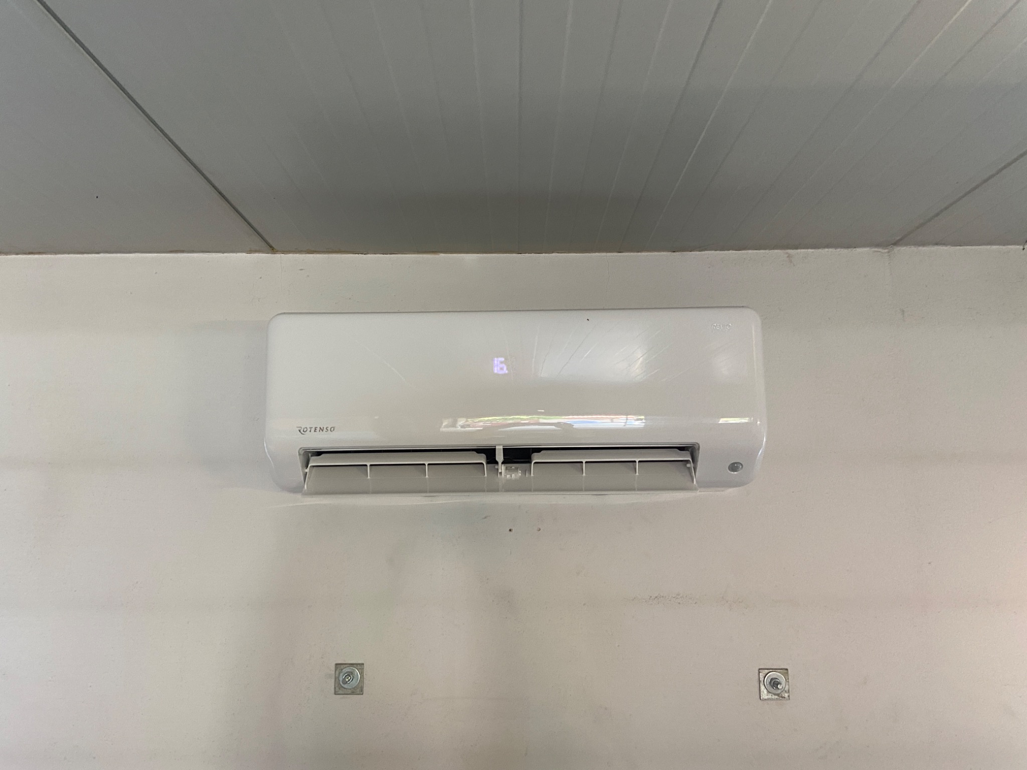 Biała jednostka klimatyzacyjna Rotenso zamontowana na pomalowanej na biało ścianie z widocznymi śladami montażu i wyświetlonym numerem 16.