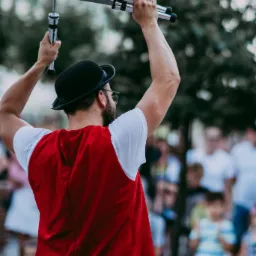 Iluzjonista w czerwonej kamizelce i meloniku prezentuje sztuczki z nożami na tle publiczności.