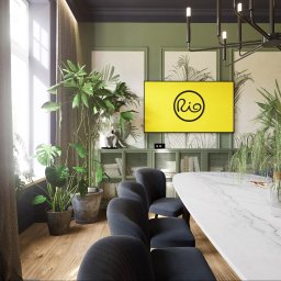 Łukasz Macuga architekt wnętrz - Elegancka sala konferencyjna z marmurowym stołem, ciemnymi krzesłami, zielonymi ścianami i roślinami doniczkowymi, oświetlona nowoczesnym żyrandolem. Na ścianie telewizor z żółtym ekranem i logo Rio.