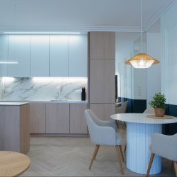 Łukasz Macuga architekt wnętrz - Jasna kuchnia z marmurowym blatem i drewnianymi szafkami, okrągły stół z krzesłami, oświetlenie LED i rośliny doniczkowe. Nowoczesny wystrój wnętrza.