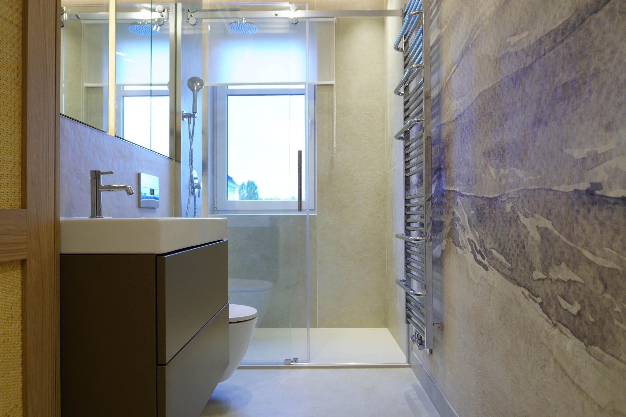 Nowoczesna łazienka z kabiną prysznicową typu walk-in, umywalką z szafką w kolorze taupe i grzejnikiem drabinkowym na ścianie z subtelnym wzorem.