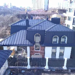 Dom z ciemnoszarym dachem z blachy na tle miejskiego krajobrazu, widok z góry ukazuje detale wykonania i estetykę pokrycia dachowego.