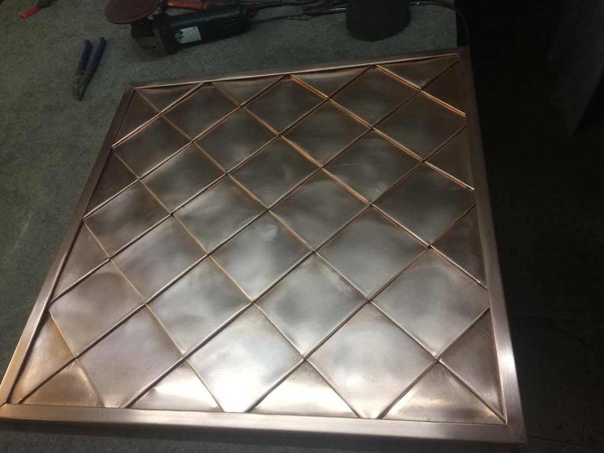 Miedziany panel dekoracyjny z kwadratowymi elementami, widoczne narzędzia blacharskie w tle.